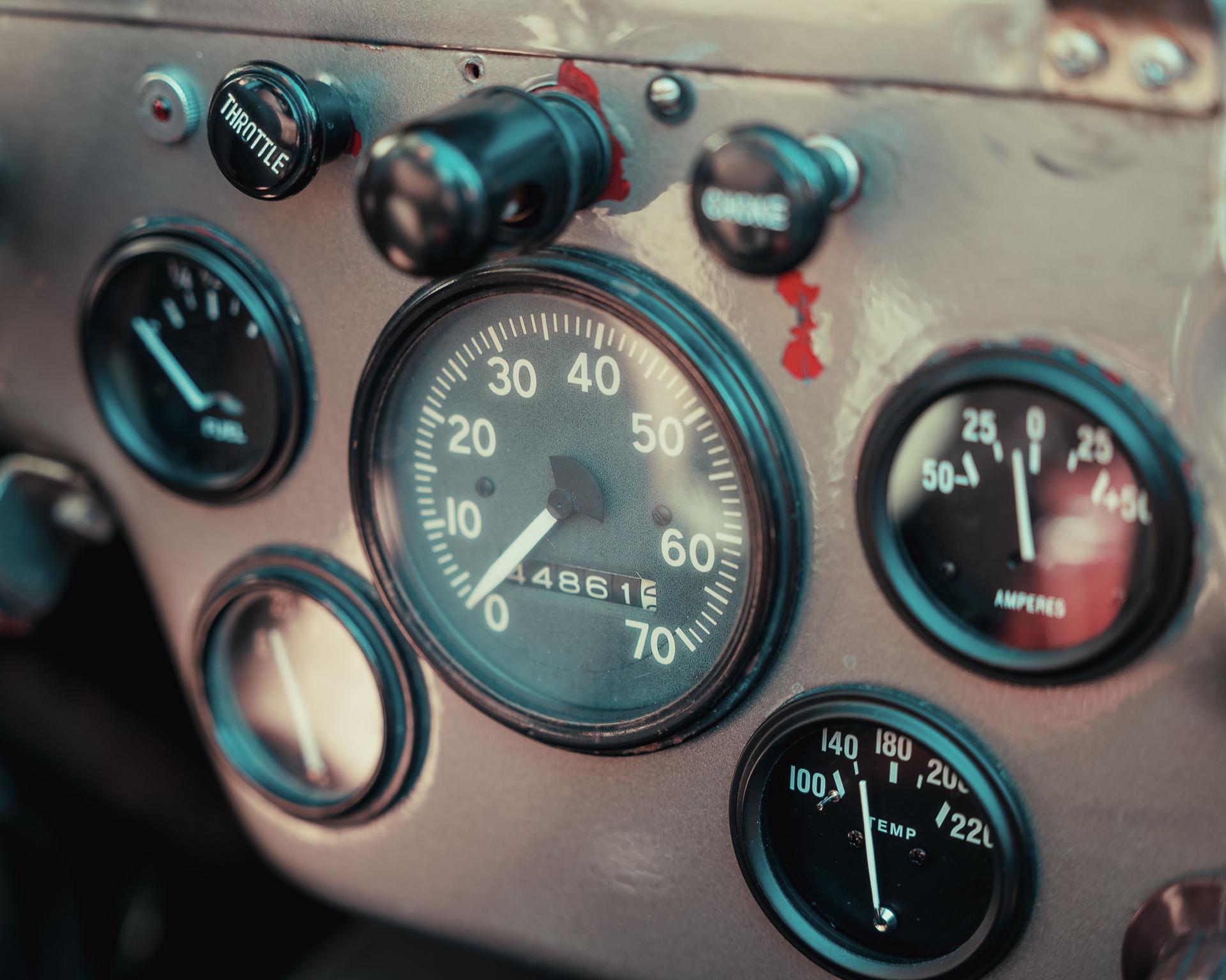 A close-up of a worn vintage instrument panel — a speedometer flanked by fuel, ampere and temperature gauges, each reading a different number